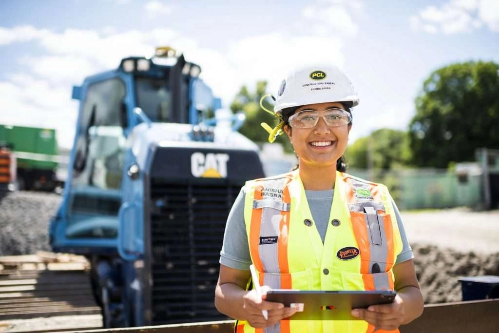 Construction worker holding tablet in front of large machinery