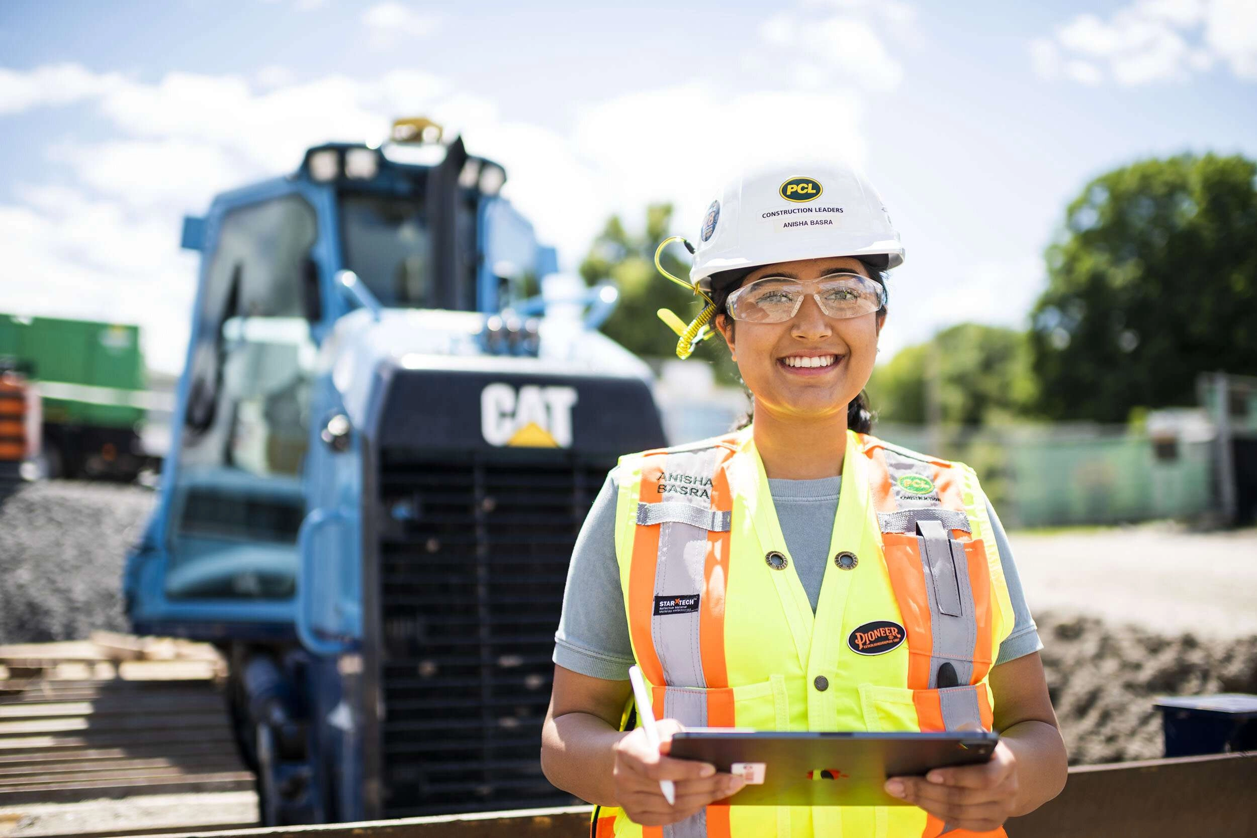 Construction worker holding tablet in front of large machinery