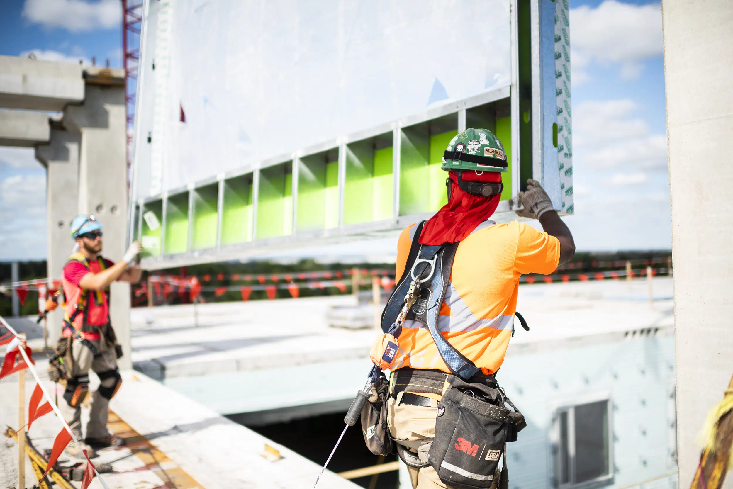 Two construction workers guide a panel as it is lowered on to a building by a crane.